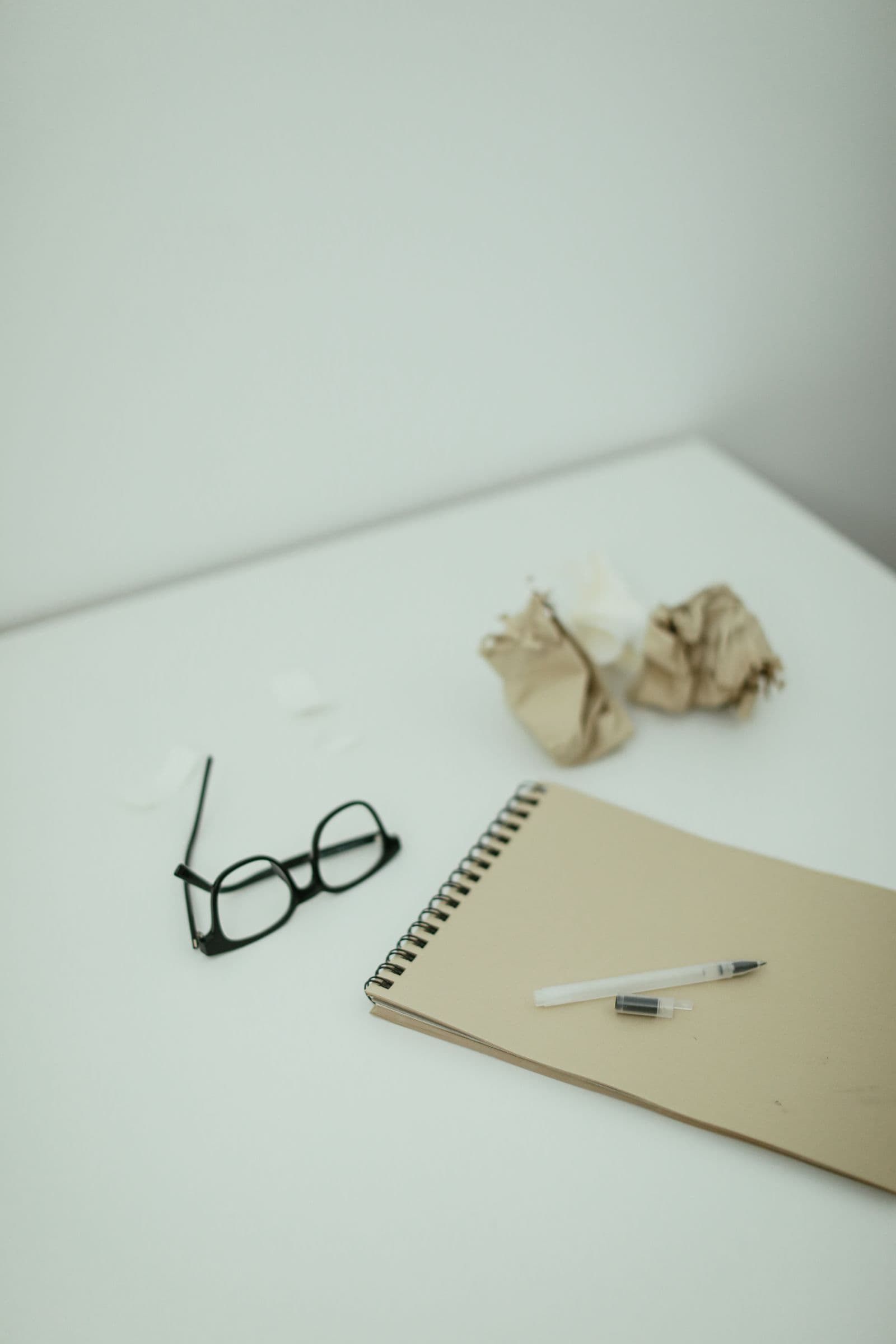 Glasses, a notebook and discarded paper on a desk